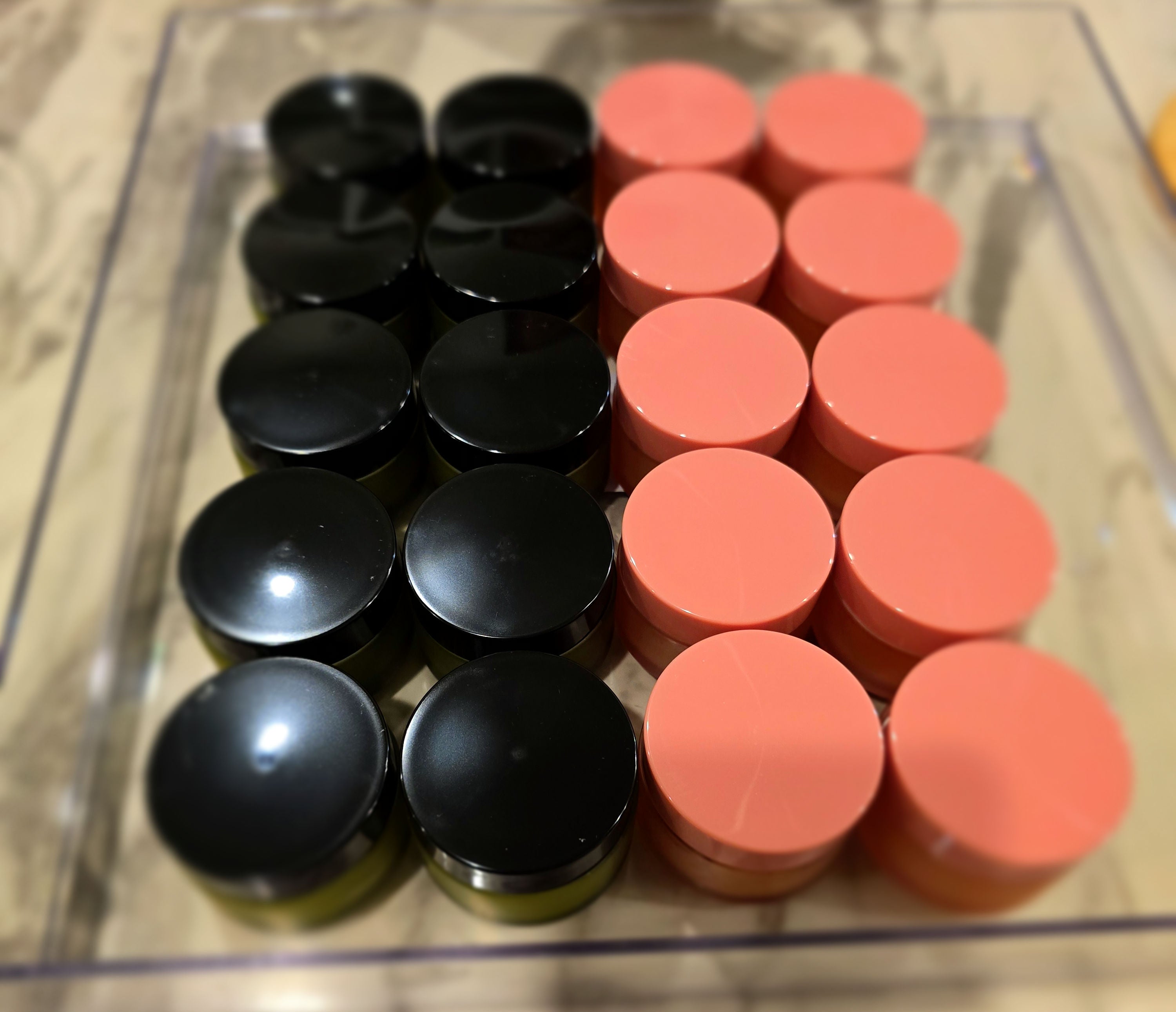 Rows of small jars with black and coral lids in clear container